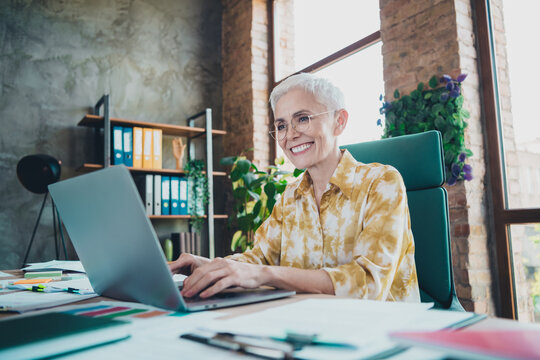 Photo of attractive senior woman working netbook wear yellow print shirt formalwear comfy modern office room interior indoors workspace