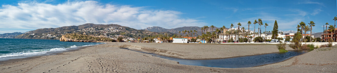 Fototapeta premium Panoramic view on the empty beach of Salobrena on the Andalusian coast in winter. In the background the castle and snowcapped Sierra Nevada.
