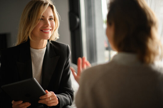 A businesswoman smiling and engaging in a face-to-face conversation with a client, listening attentively and explaining, reflecting professionalism and friendly communication.