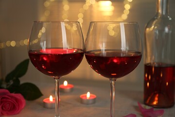 Romantic place setting with red wine, burning candles and rose on table against blurred lights,...