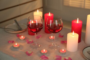 Romantic place setting with red wine, burning candles and petals on table