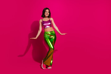Stylish young woman in bright glossy clothing dancing against vivid magenta background