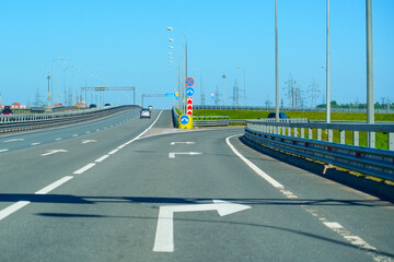 A well-maintained highway stretches into the distance, flanked by green grass. Important guide signs are clearly visible right exit arrow, providing direction to drivers