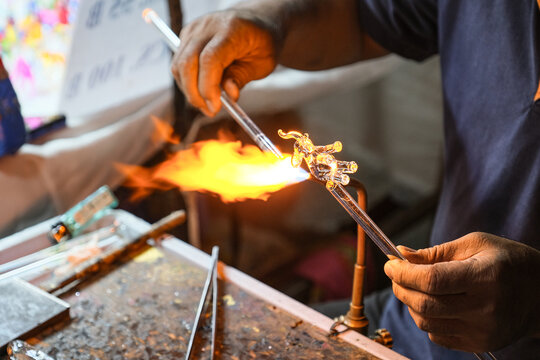 Creating glass art with hot torch and glassblowing pipe. The process of glass making, Glassblower shaping the red melted glass, A glass blower melting glass