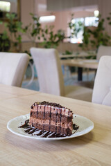 A decadent slice of chocolate layer cake drizzled with chocolate sauce sits on a white plate