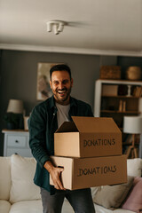 The smiling man is holding and packing boxes with gently used clothes for charity.