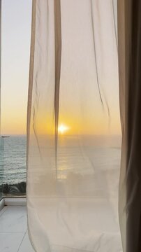 vertical video of colourful sunset golden hour from a hotel transparent glass balcony to Mediterranean Sea of greek cyprus island with curtains moving in the wind