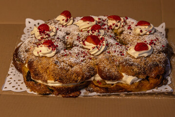  A delicious festive cake topped with whipped cream, fresh strawberries, powdered sugar, and crushed dried raspberries, displayed on a doily.