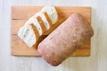 A loaf of bread sliced and ready to eat sits on a wooden cutting board