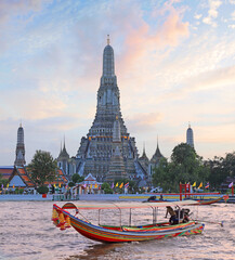 Wat Arun Temple at sunset with traditional boat on the river on the foreground, Bangkok, Thailand