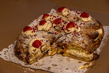  A sliced festive cake filled with cream, topped with strawberries, powdered sugar, and crushed raspberries, displayed on a decorative doily.