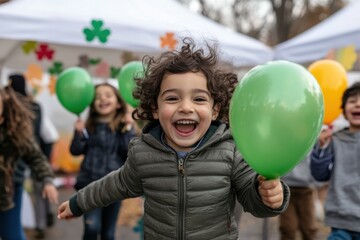 A happy child with curly hair runs joyfully, holding green balloons, embodying the spirit of fun and innocence at an outdoor celebration.