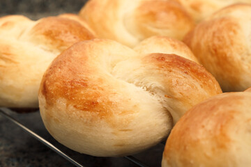 Bread buns on cooling rack. Close up. Baked yeast bread knots in a row. Braided knot rolls. Traditional Swiss butter bread called Zopf or Challah prepared for holiday meals. Selective focus.