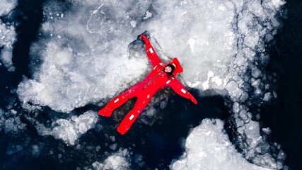 Aerial view of man ice floating on icy water in bright red survival suits. Arctic frozen landscape. Extreme adventure, ice diving, cold water survival, winter expedition. Fun, outdoor activity © velirina