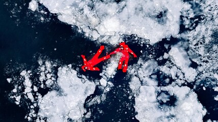 Fototapeta premium Aerial view of two people ice floating on icy water in bright red survival suits. Arctic frozen landscape. Extreme adventure, ice diving, cold water survival, winter expedition. Fun, outdoor activity