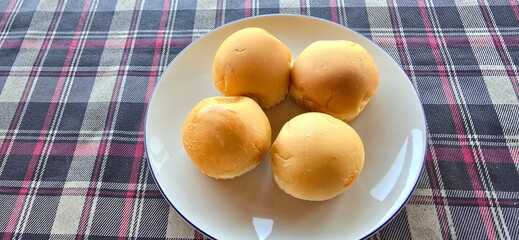Top view of homemade round breads 4 (Inside is filled with green pandan custard filling) arranged on white plate. Bread plate on red-black plaid tablecloth background. Brioche buns weet and good smell