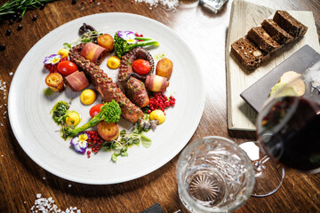 Grilled octopus tentacles with cherry tomatoes, broccoli, and edible flowers. Served with roasted potatoes, yellow sauce, and microgreens. Gourmet seafood dish in a modern restaurant