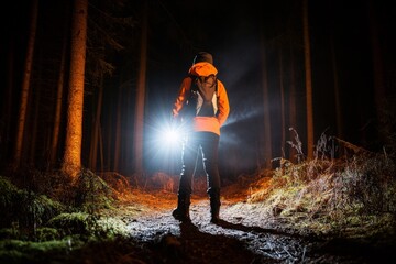 Obraz premium A person standing nervously at the edge of a forest trail, clutching a flashlight and hesitating to take the first step