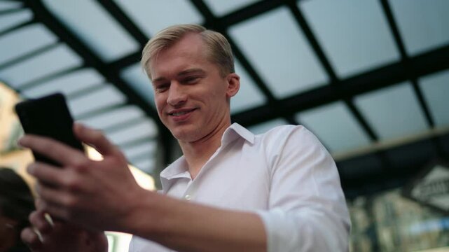 Smiling Caucasian young male focused on interacting with smartphone, exploring mobile app. Satisfied man enjoys carefree moments outdoors, typing messages or completing tasks using digital technology
