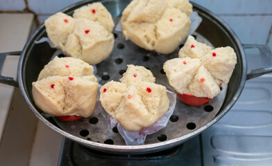 Steaming basket with Huat Kueh (Chinese prosperity cakes). Light yellow, split-top cakes with red dots, nestled on paper liners.  Ready for serving. Blue patterned background.