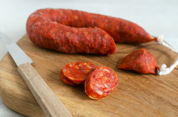 Spanish Chorizo sausage with red pepper, paprika and garlic on a wooden cutting board with a knife. Traditional Mediterranean food concept. Horizontal orientation. Selective focus.