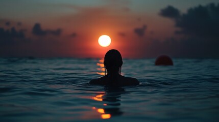 A silhouette of a person wading in the ocean at sunset, with vibrant colors reflecting on the water.