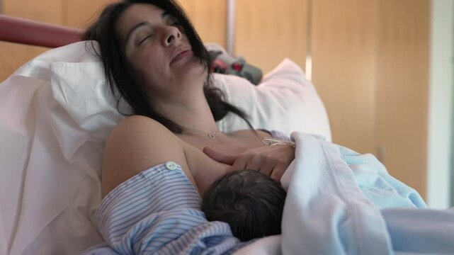 New mother struggles with breastfeeding pain after giving birth to baby seated at hospital bed, childbirth maternal care and breast pain
