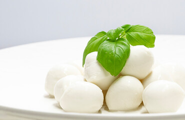 Homemade food, snow-white mozzarella balls, and basil, on parcel plates and an unusual background.
