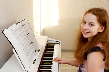 happy red-haired girl sitting at digital piano at home