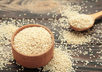 Raw sesame seeds in wooden bowl and spoon on brown wooden background.
