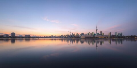 Fototapeta premium Panoramic view of Montreal skyline during sunset with reflection in the calm waters of a lake or river, soft pastel hues dominating the sky, building, calm