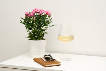 An Elegant and Stylish Table Setting with a glass of wine, beautiful, fresh flowers in a pot, notebook, glasses on white table in light room.
