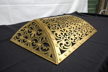 Sheet metal shape with golden color and pattern on black surface, decorative item, abstract design, sculpture, gold