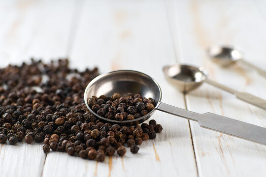 black pepper seeds spilled from a teaspoon on a light kitchen table, selective focus.