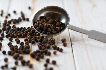 black peppercorns in a measuring spoons on a white wooden table, selective focus.