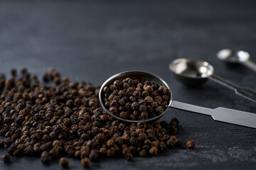 black peppercorns in a measuring spoons on a black kitchen table, selective focus.