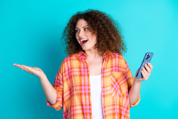 Young woman gesturing with excitement while holding a smartphone against a vibrant teal background