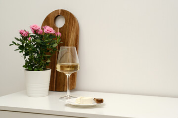 An Elegant and Stylish Table Setting with a glass of wine, cheese on plate, beautiful, fresh flowers in a pot on white table in light room.