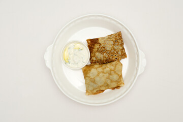 Delicious rolled crepes with mushrooms with sour cream jn white plate in bright background, closeup