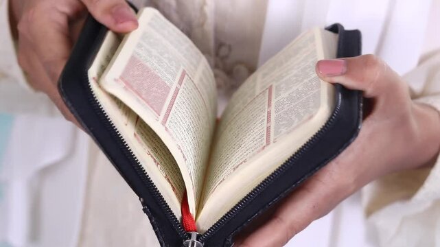 Close up of hands turning the pages of a book quran with Arabic scrip, showcasing printed text, the black book cover is visible, isolated on a green background or green screen