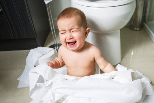 Toddler ripping up toilet paper in bathroom