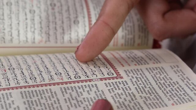 A person's finger points to a verse in the Quran with Arabic scrip, with the book opened to a page displaying Arabic script. isolated on a green background or green screen