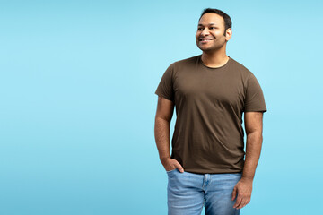 Middle aged indian man smiling and looking away on blue background