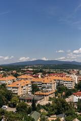 Uzhhorod cityscape with colorful buildings and lush greenery, under a blue sky with white clouds, showcasing the beauty of the carpathian mountains in the background on a sunny summer day