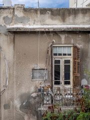An old peeling wall with a wooden window and open shutters. A small balcony with metal railings and...