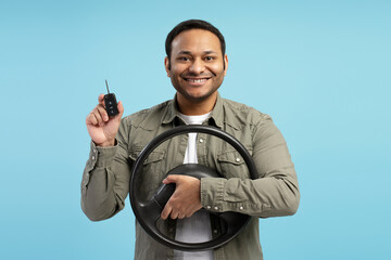 Happy driver holding steering wheel and car key on blue background