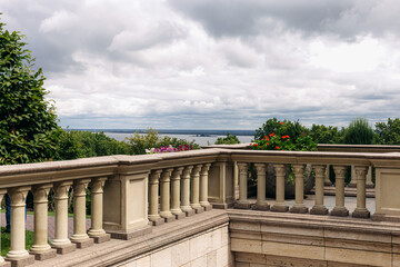 Stone balustrade bordering terrace with blooming potted flowers, framing tranquil lake beneath...