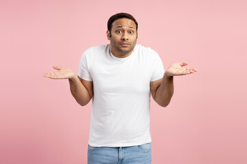 Puzzled man shrugging shoulders on pink background: clueless expression