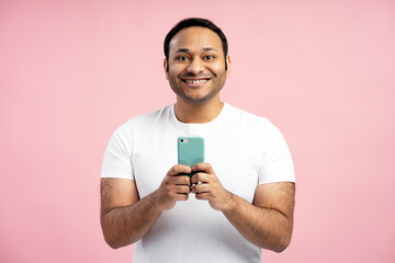 Smiling middle aged man using smartphone on pink background