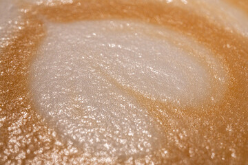 Macro shot of creamy cappuccino foam with sparkling bubbles and a smooth texture in warm golden tones